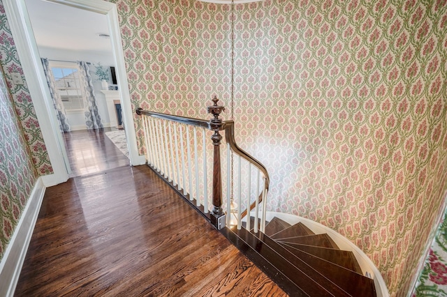 stairway with baseboards, wood finished floors, a fireplace, and wallpapered walls