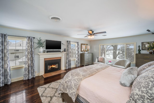 bedroom featuring a glass covered fireplace, multiple windows, visible vents, and hardwood / wood-style floors