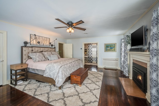 bedroom with crown molding, baseboards, radiator heating unit, wood finished floors, and a glass covered fireplace