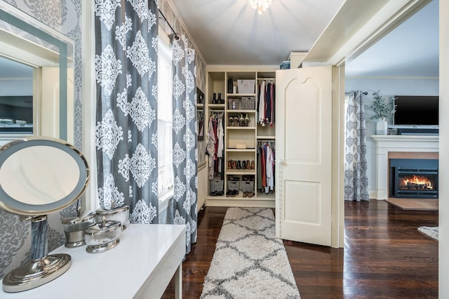 bathroom featuring a walk in closet, crown molding, wood finished floors, and a warm lit fireplace