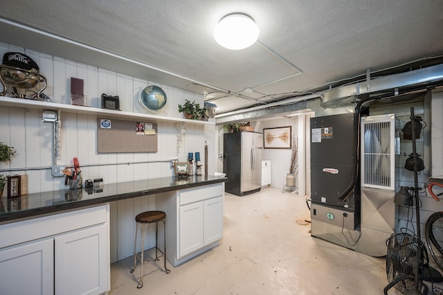 basement with heating unit, a textured ceiling, and freestanding refrigerator