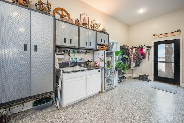 kitchen with a sink, light speckled floor, dark countertops, freestanding refrigerator, and white cabinets