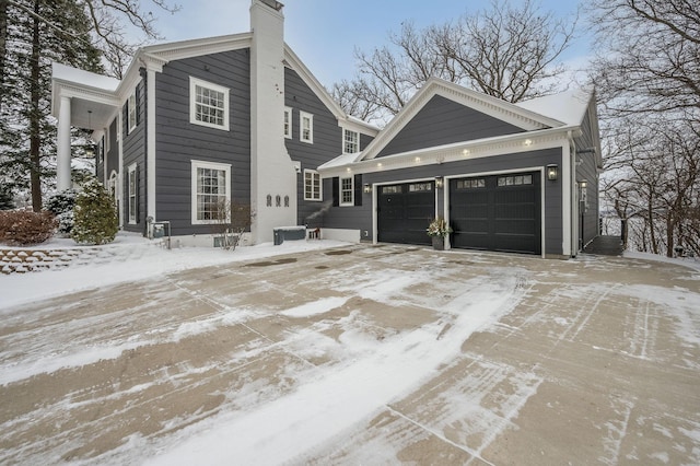 view of snow covered exterior featuring driveway, an attached garage, and a chimney