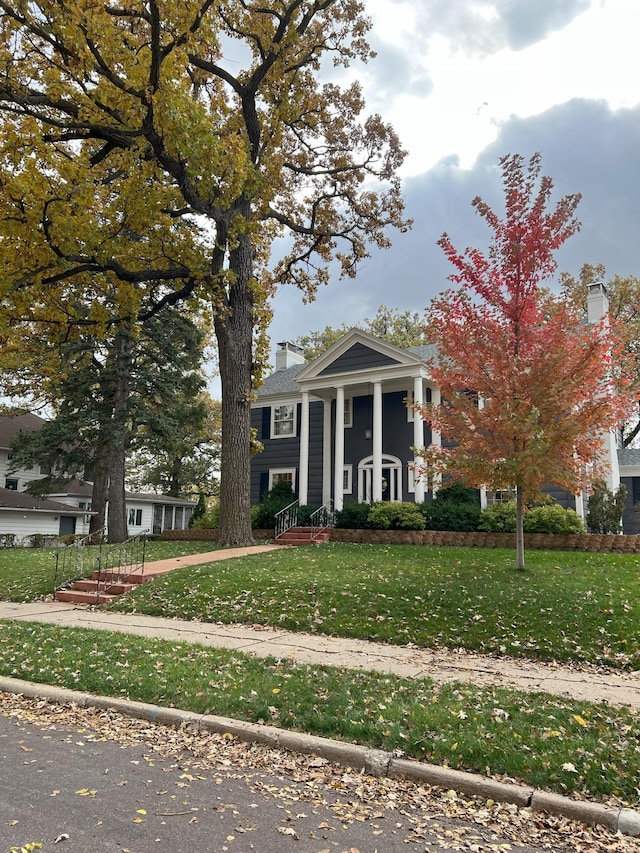 neoclassical home featuring a chimney and a front yard