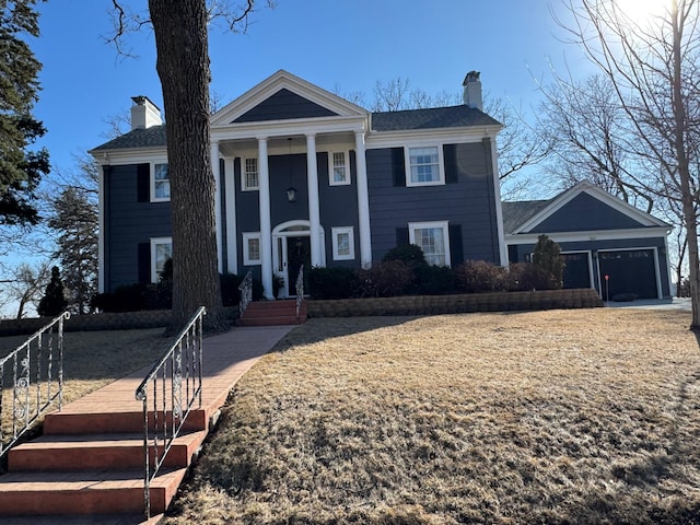 neoclassical home featuring an attached garage and a chimney