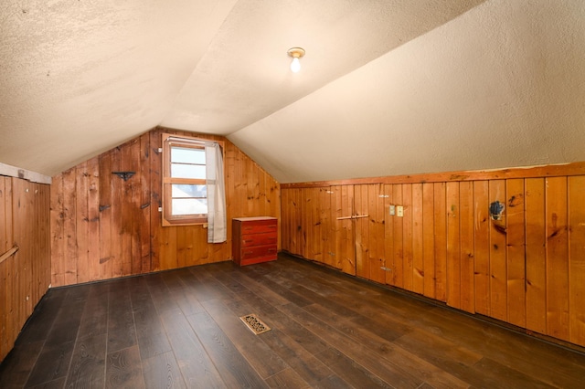 bonus room with wood walls, lofted ceiling, and dark wood-type flooring