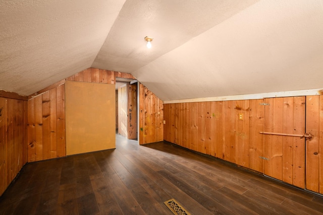 bonus room featuring a textured ceiling, lofted ceiling, wooden walls, and dark hardwood / wood-style floors