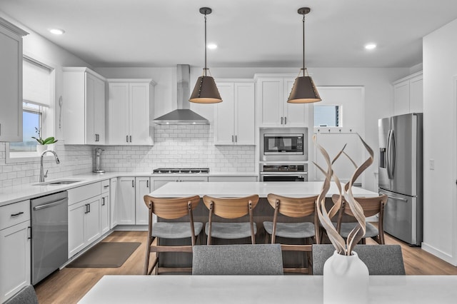 kitchen featuring sink, wall chimney exhaust hood, hanging light fixtures, stainless steel appliances, and tasteful backsplash