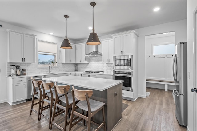 kitchen featuring white cabinets, light hardwood / wood-style flooring, pendant lighting, a kitchen island, and appliances with stainless steel finishes