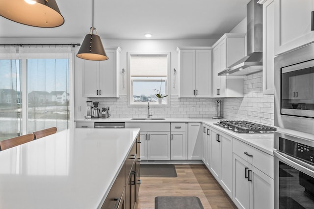 kitchen featuring white cabinets, decorative light fixtures, wall chimney range hood, and appliances with stainless steel finishes