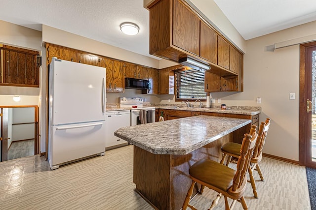 kitchen with white appliances, sink, a textured ceiling, kitchen peninsula, and a breakfast bar area