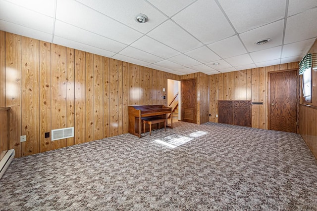 carpeted spare room with a paneled ceiling and wood walls