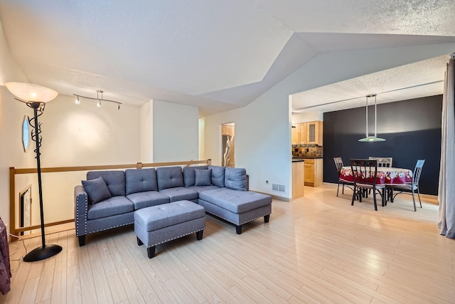 living room with lofted ceiling, a textured ceiling, and light hardwood / wood-style flooring