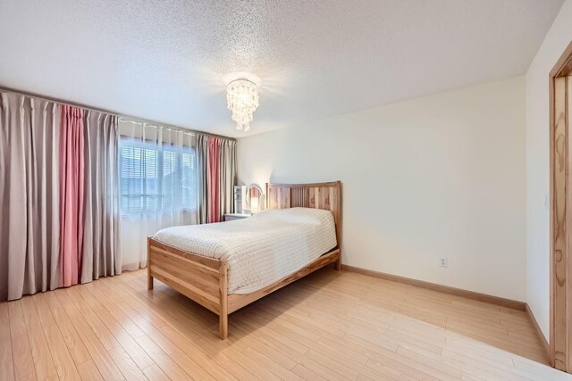 bedroom featuring light hardwood / wood-style floors, a textured ceiling, and an inviting chandelier