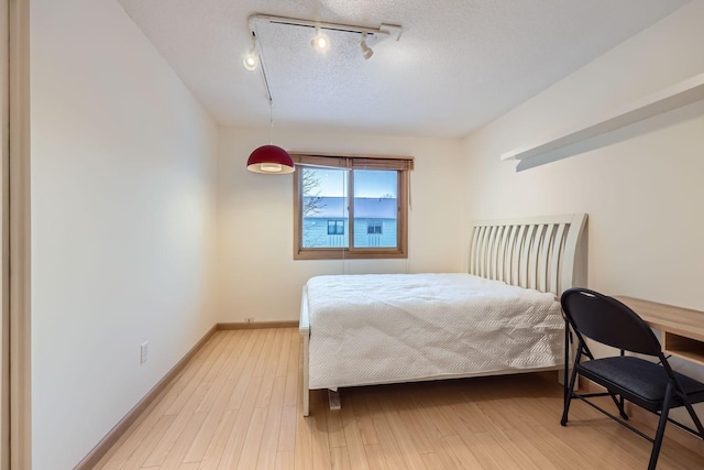 bedroom featuring light hardwood / wood-style flooring, rail lighting, and a textured ceiling