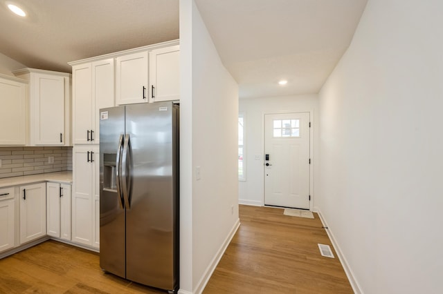 kitchen with white cabinets, stainless steel fridge with ice dispenser, light wood-type flooring, and tasteful backsplash