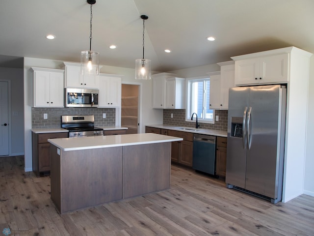 kitchen featuring appliances with stainless steel finishes, light wood-type flooring, a kitchen island, white cabinetry, and hanging light fixtures