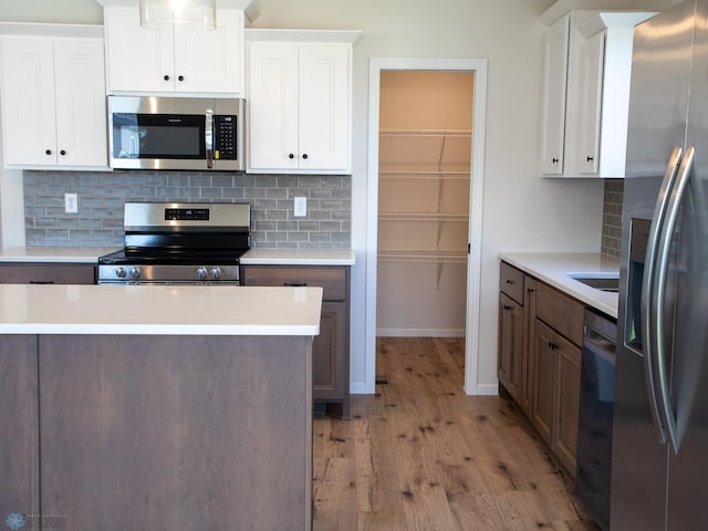 kitchen featuring appliances with stainless steel finishes, light wood-type flooring, tasteful backsplash, dark brown cabinetry, and white cabinetry