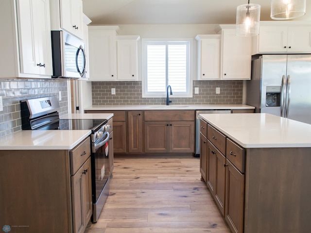 kitchen with sink, appliances with stainless steel finishes, decorative light fixtures, light hardwood / wood-style floors, and white cabinetry