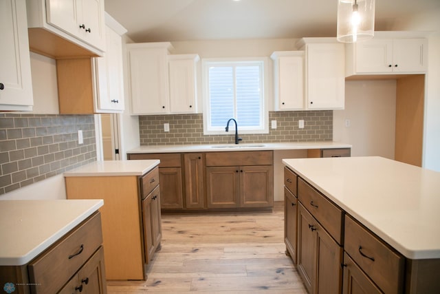 kitchen featuring backsplash, sink, light wood-type flooring, a kitchen island, and white cabinetry