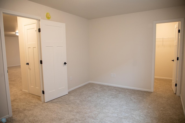 unfurnished bedroom featuring a walk in closet, light carpet, and a closet