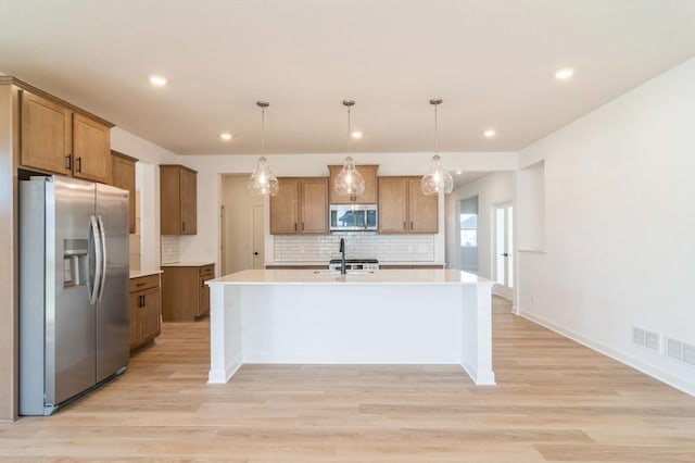 kitchen with a center island with sink, light hardwood / wood-style floors, decorative light fixtures, and appliances with stainless steel finishes