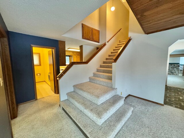 staircase featuring vaulted ceiling, carpet, wooden ceiling, and a textured ceiling