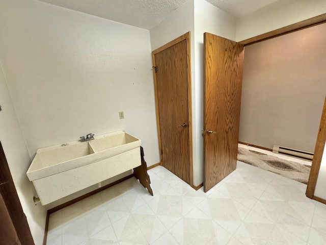 bathroom featuring a textured ceiling, a baseboard heating unit, and sink