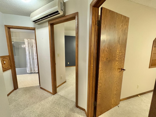 hall with a wall mounted air conditioner, light colored carpet, and a textured ceiling