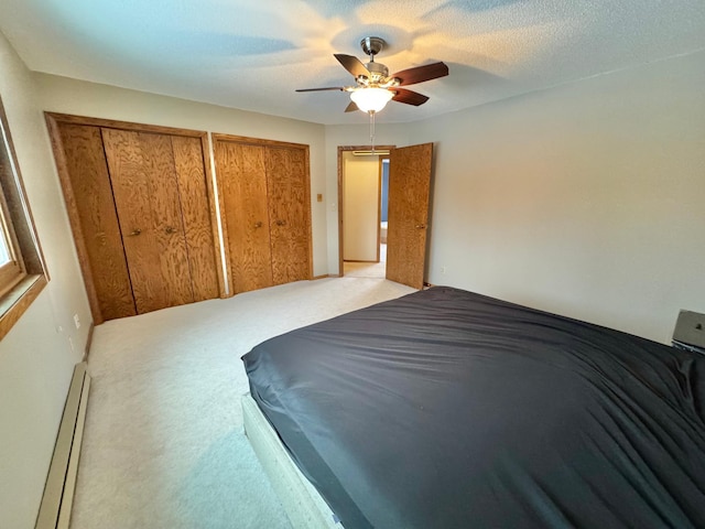 bedroom featuring two closets, ceiling fan, a textured ceiling, baseboard heating, and light colored carpet