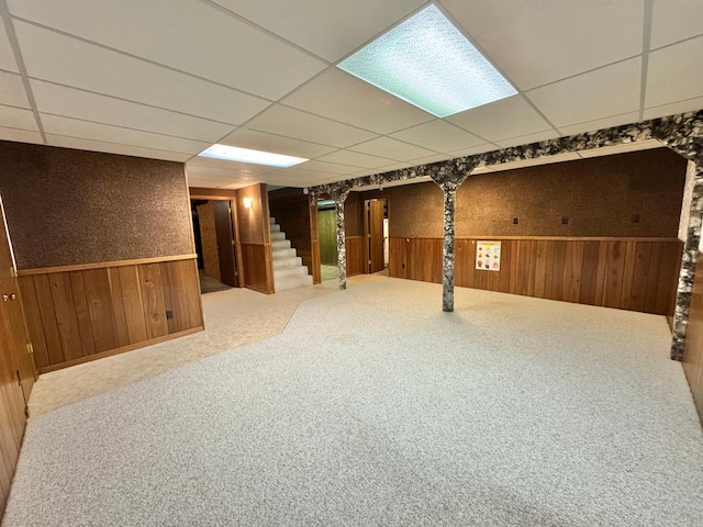 basement with wooden walls, a drop ceiling, and carpet