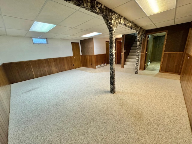 basement with baseboard heating, wood walls, a drop ceiling, and carpet floors