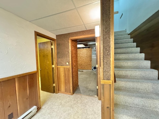 stairway with carpet flooring, a paneled ceiling, wood walls, and a baseboard heating unit