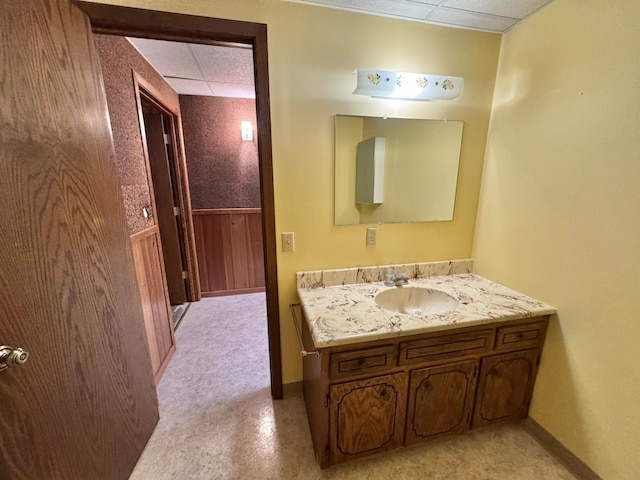 bathroom with vanity, a drop ceiling, and wooden walls