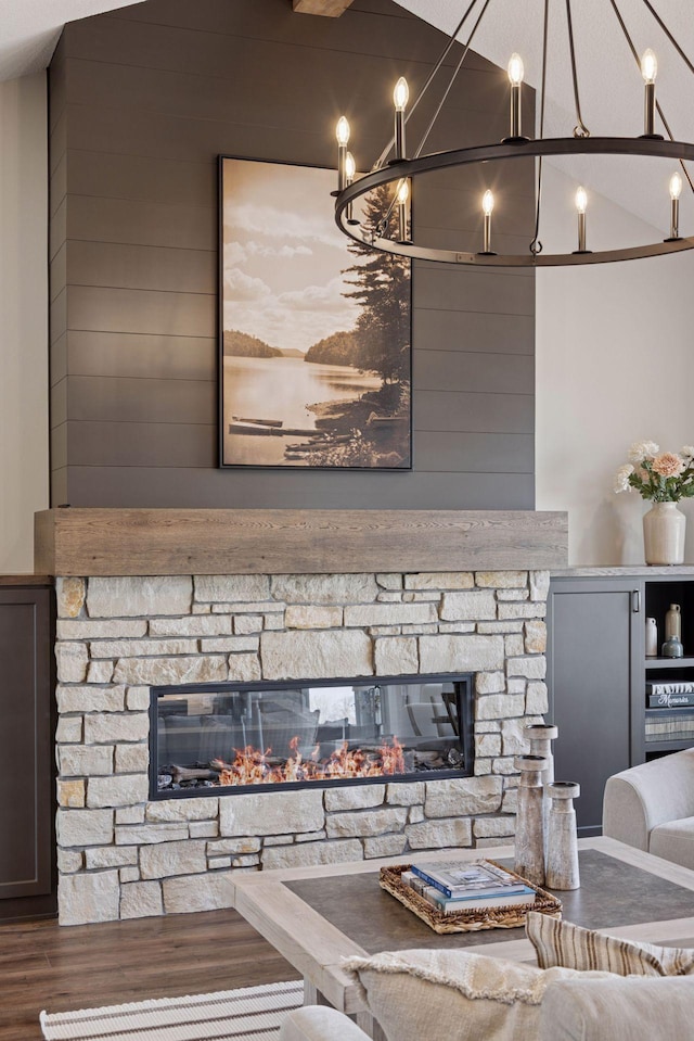 living area with a stone fireplace, wooden walls, wood finished floors, vaulted ceiling, and an inviting chandelier