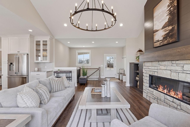 living area featuring baseboards, dark wood-type flooring, vaulted ceiling, a stone fireplace, and recessed lighting