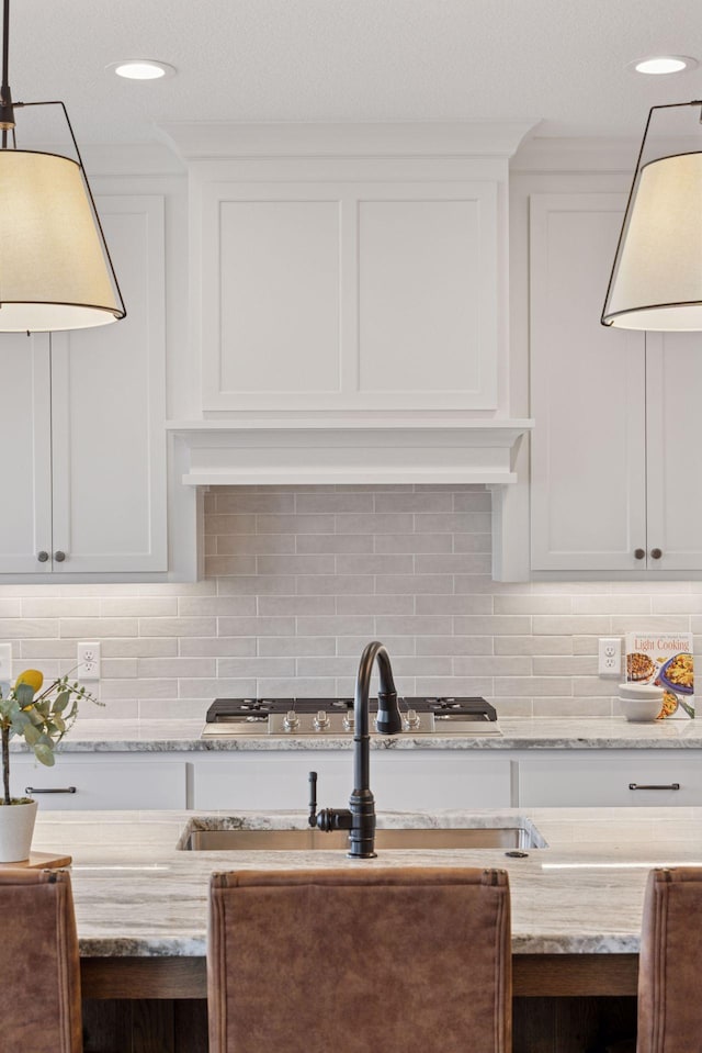 kitchen with white cabinetry, decorative light fixtures, decorative backsplash, and light stone countertops