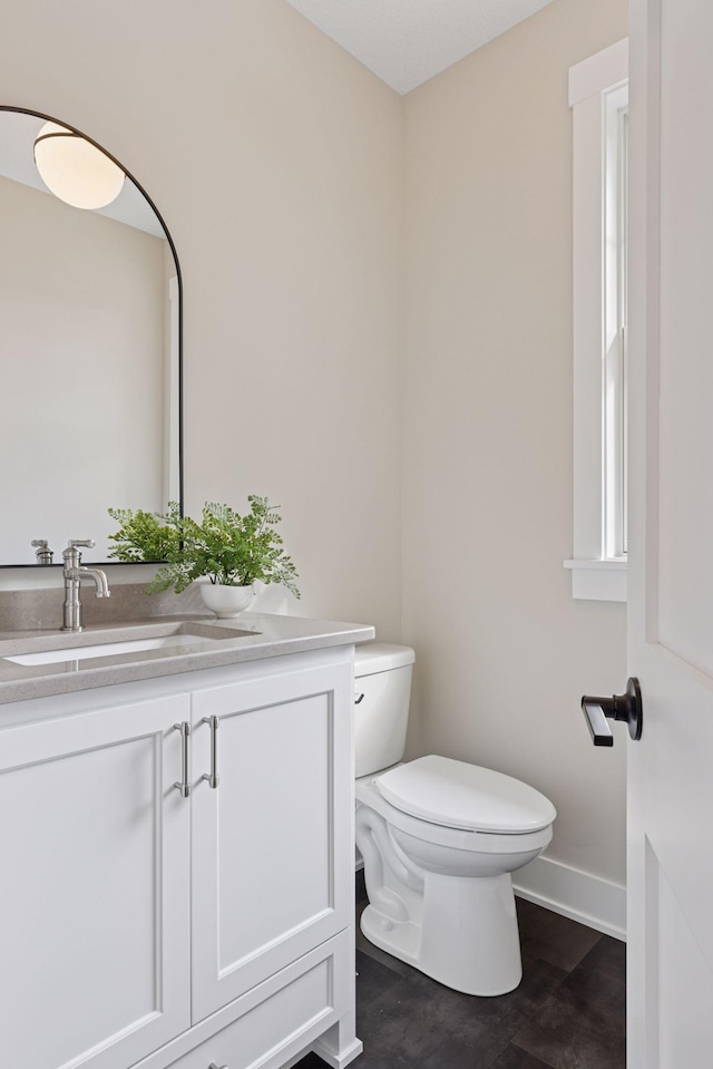 half bathroom featuring vanity, toilet, and baseboards