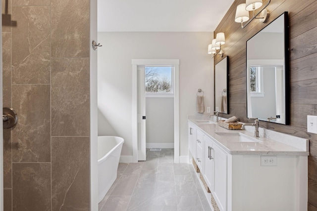 full bathroom with a freestanding bath, double vanity, a sink, and baseboards