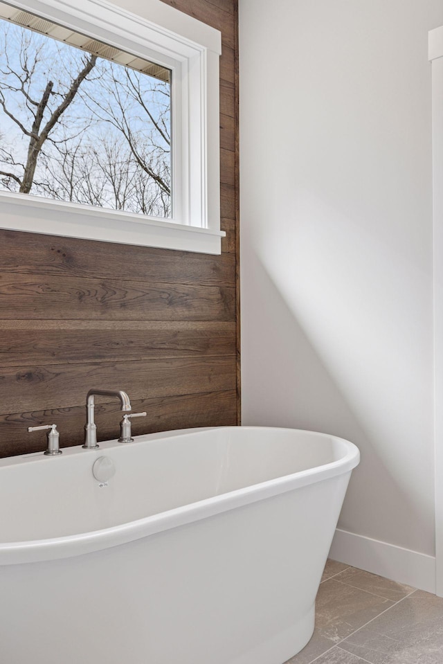 bathroom with a soaking tub, baseboards, and wood walls