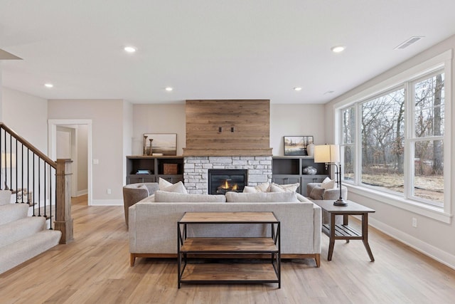 living area featuring light wood finished floors, visible vents, baseboards, stairway, and a stone fireplace