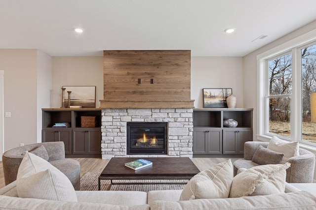 living room featuring a stone fireplace, light wood-type flooring, visible vents, and recessed lighting