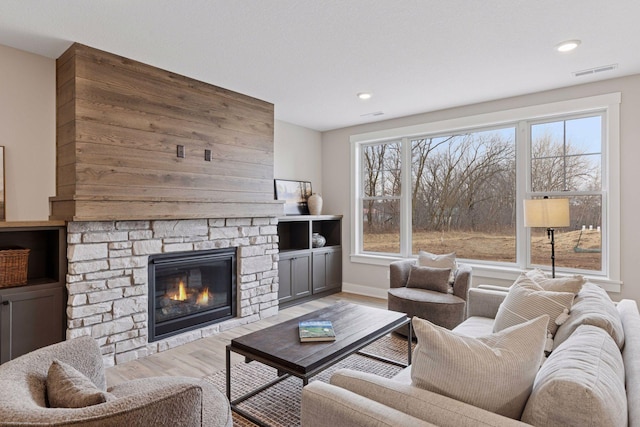 living room with a stone fireplace, wood finished floors, visible vents, and baseboards