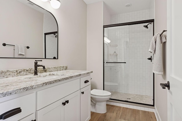 bathroom with toilet, a shower stall, wood finished floors, and vanity