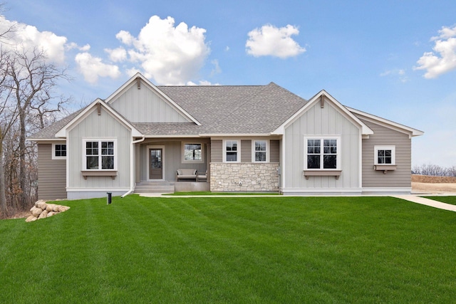 view of front of home with stone siding, a shingled roof, board and batten siding, and a front yard