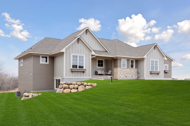 rear view of house with stone siding, roof with shingles, board and batten siding, and a yard