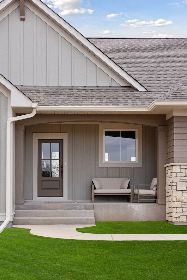 entrance to property with stone siding, a shingled roof, board and batten siding, and a yard