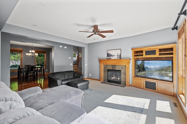 carpeted living room with a tiled fireplace and ceiling fan with notable chandelier