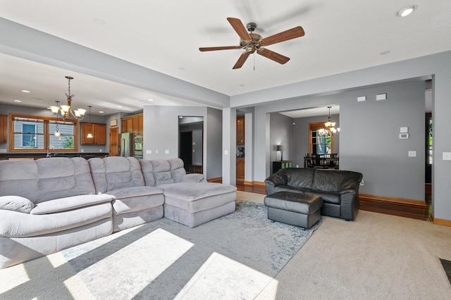 living room with light carpet, sink, and ceiling fan with notable chandelier