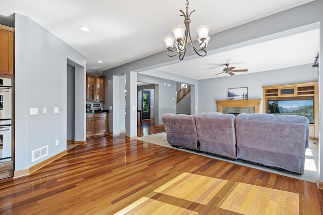 living room featuring ceiling fan with notable chandelier, wood-type flooring, a wealth of natural light, and a tiled fireplace